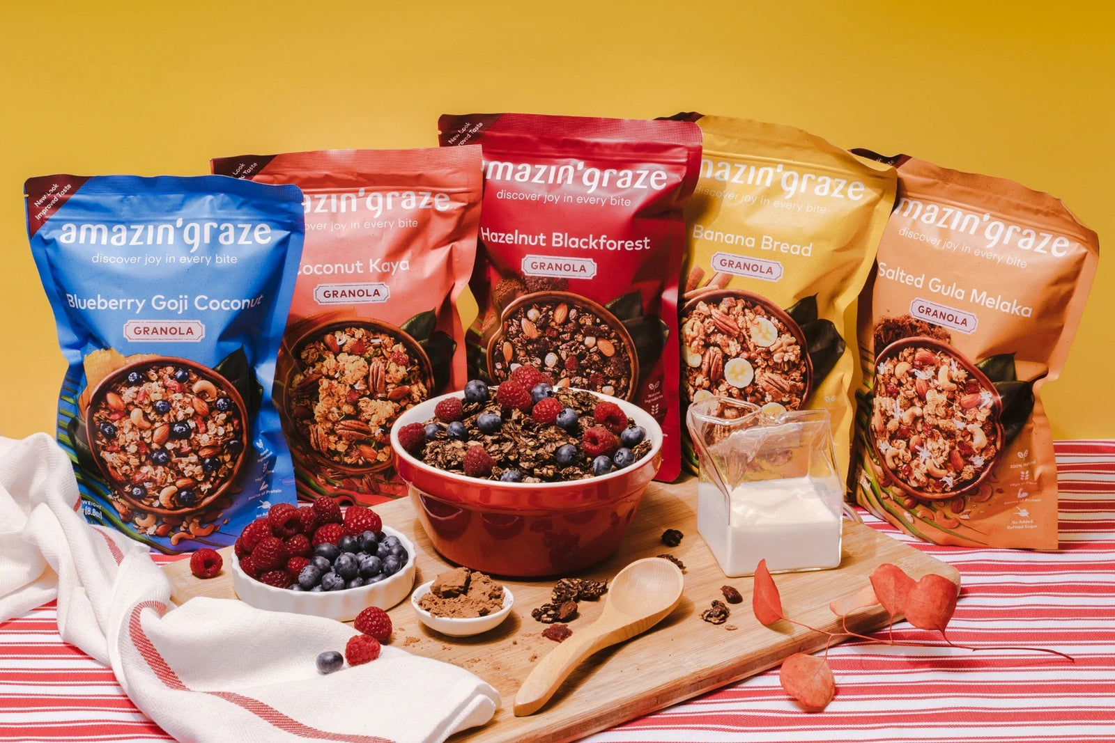 Amazin’ Graze granola varieties displayed with berries, milk, and a breakfast bowl.