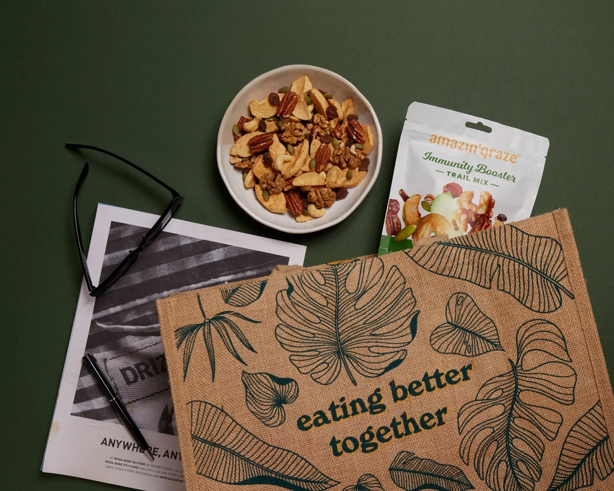 Amazin' Graze Immunity Booster Trail Mix package with bowl of mixed nuts and dried fruit on green surface.